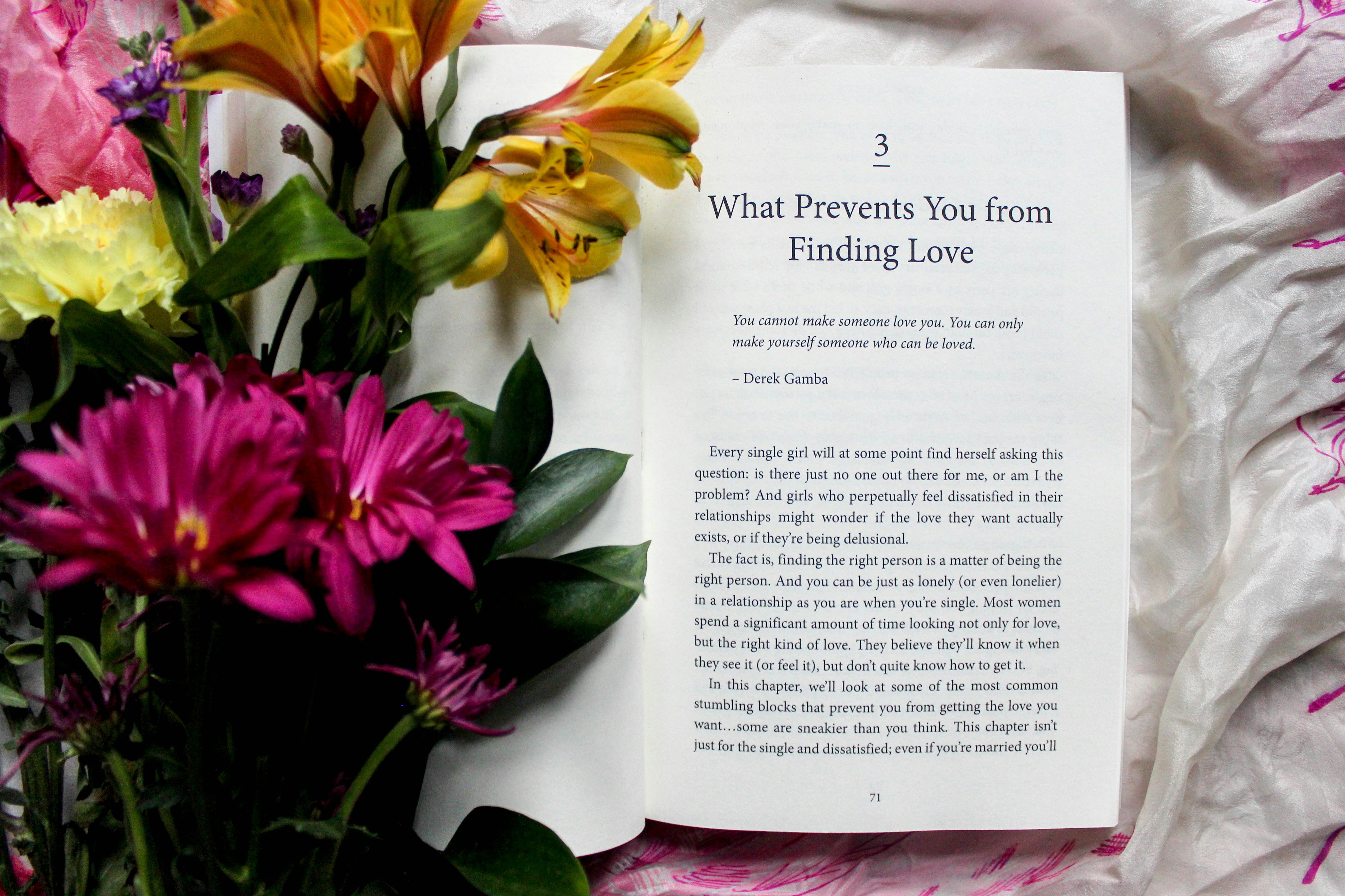 reading book beside pink, yellow, and green petaled flower bouquet